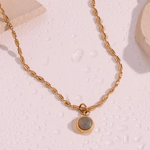 Macro detail of 18K gold-plated olive bead chain with grey natural stone pendant