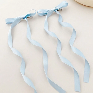 Detailed view of light blue ribbon bow hair clips with long wavy streamers on silk fabric