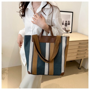 Detail of striped canvas tote bag featuring leather handles and reinforced base corners