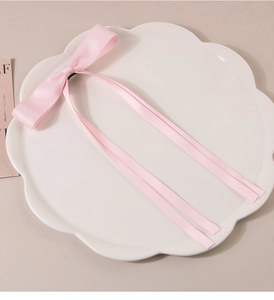 Detailed view of a sweet pink satin bow hair clip with long ribbons on a ceramic plate