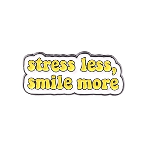 Détail du pin's émaillé avec texte 'stress less, smile more' en typographie jaune