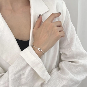 Detail of silver link chain bracelet with interlocking letters on a white fabric sleeve