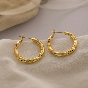 Detail of gold C-shaped hoop earrings with hammered metal texture on soft beige fabric