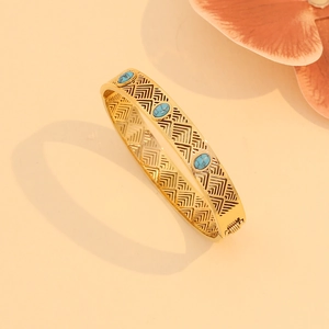 Vintage gold hollow-out bangle with three oval turquoise stones on a soft background