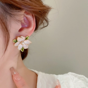 Close-up of pearl flower stud earrings with white enamel petals and green leaf on ear