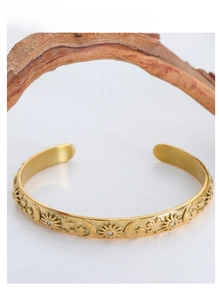Close-up of gold open bangle featuring embossed sun, moon, and star designs with zircon