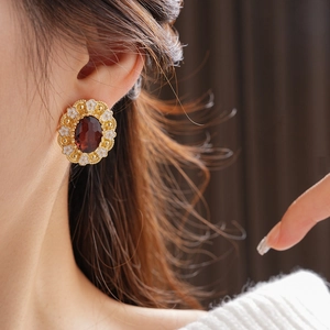 Detail of vintage gold earrings with deep red oval gemstone and white enamel flowers