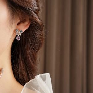Detail of colorful bow earrings with a purple teardrop crystal on a female model