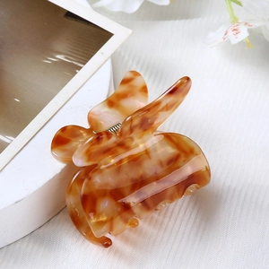 Detail of tortoise shell brown acetate hair claw clip on white textured fabric background