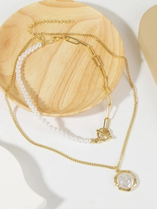 Detail of layered gold chain with white baroque pearls and round relief pendant on wood