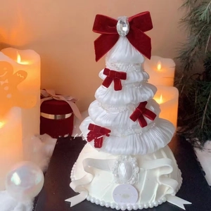 Macro shot of white tiered fabric Christmas tree with pearls and red velvet bows decoration