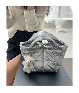 Detail of silver quilted puffer handbag with metallic finish and white bear keychain charm