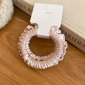 Vue détaillée de la texture du chouchou en satin rose sur une surface en bois