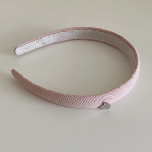 Détail d'un serre-tête tricoté rose avec un petit pendentif en métal argenté en forme de cœur