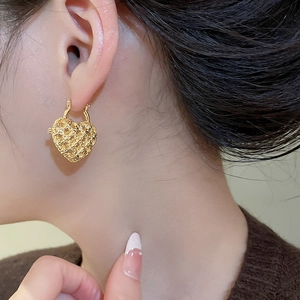 Close-up of vintage hollow heart earrings in gold metal on model ear for elegant style
