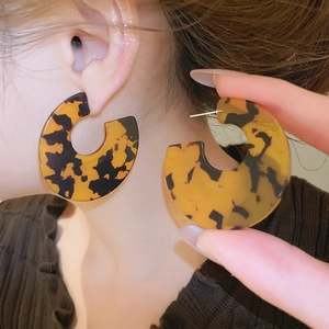 Macro detail of large C-shaped acrylic earrings with retro tortoise shell texture patterns