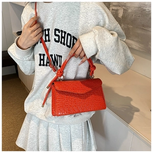 Detail of orange crocodile pattern PU leather handbag with twisted handle and gold hardware