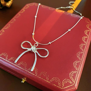 Close-up of silver titanium bow pendant necklace displayed on a jewelry box