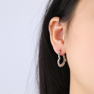 Boucles d'oreilles cœur en acier inoxydable argenté avec détails perlés sur modèle