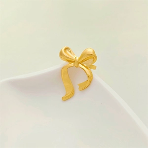 Close-up of matte gold bow-shaped ring with a silky 3D texture on white ceramic