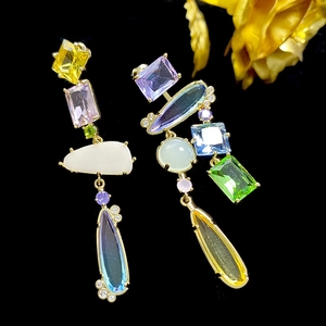 Asymmetric gold dangle earrings with multi-colored crystals on a black background