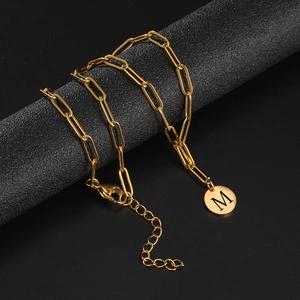 Detail of gold paperclip chain necklace with round letter M pendant on black display