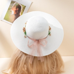 Detail of white wide brim straw hat with floral wreath and pink ribbon bow on model