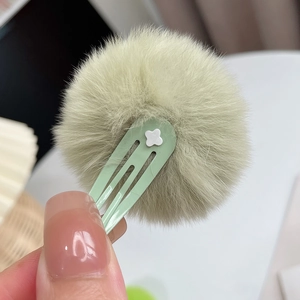 Close-up of a soft light green faux fur pom pom hair clip with small clover detail