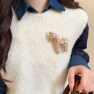 Detailed view of horse-shaped fabric brooch with floral embroidery on a white sweater