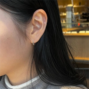 Close-up of a minimalist silver hexagonal hoop earring worn on a female ear