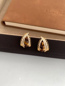 Detailed macro view of gold-plated arch earrings with tiger eye beads and pavé zircons