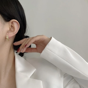 Close-up of golden irregular hammered texture stud earrings on model in white suit