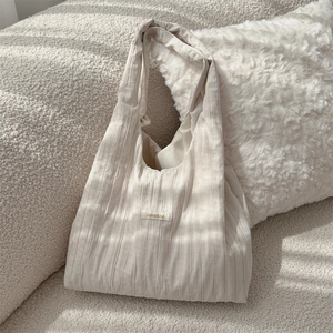 Detailed close-up of cream white pleated fabric tote with vertical texture and logo label