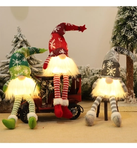Three glowing knitted Christmas gnomes with LED lights on a miniature snowy winter scene
