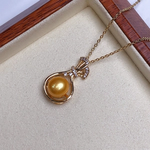 Macro detail of a round golden pearl pendant with sparkling zircon ribbon on a velvet box
