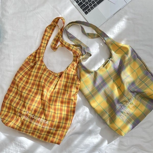 Detail shot of embroidered reusable canvas tote bags with vibrant plaid patterns and text
