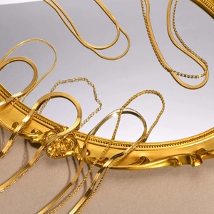 Artistic close-up of double layer 18k gold snake bone and flat link necklaces on a mirror