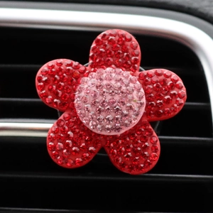 Close-up of a sparkling red rhinestone flower car air vent clip on a black dashboard