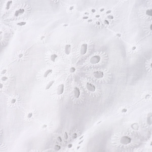 Detailed macro view of white cotton fabric with intricate floral cutout embroidery texture