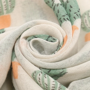 Close-up of soft breathable beige muslin scarf with green and orange cactus print texture