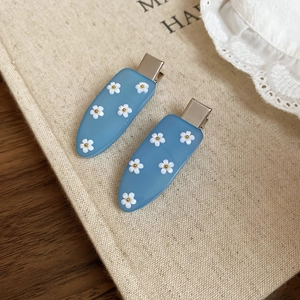 Close-up of light blue candy-colored hair clips with white flower patterns on beige linen