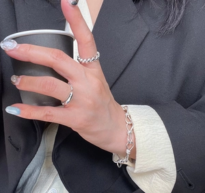 Close-up of minimalist silver rings and knot bracelet on hand holding a coffee cup