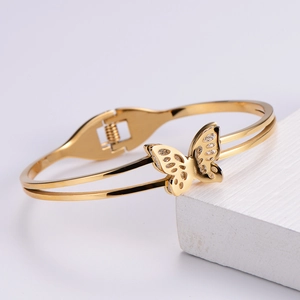 Detailed view of an open golden butterfly bangle on a white textured display block
