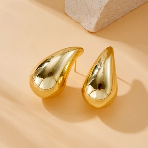 Vue macro de boucles d'oreilles goutte d'eau dorées polies sur pierre avec ombre douce