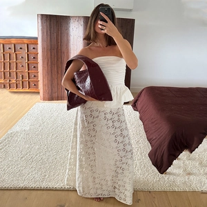 Detailed view of white lace maxi skirt styled with a matching tube top and red handbag