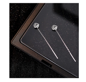 Dettaglio macro di eleganti orecchini a filo con rosa d'argento e finitura metallica fine