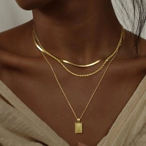 Close-up of layered gold tone necklaces including snake chain and square pendant on a model