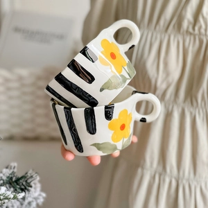 Close-up of hand-held stackable ceramic mugs with hand-painted yellow floral and black stripes