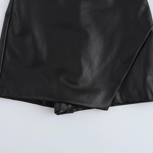 Detailed macro view of black PU leather fabric texture and pleated hem on a chic skort