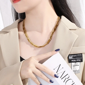 Detail view of gold-plated rectangular box chain necklace on a model wearing a blazer